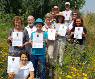 Wildkräuterbotschafterinnen und -botschafter mit Zertifikat auf einer Wiese inmitten von Wildkräutern